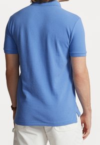 Polo shirt azzurro chiaro con tessuto texture, maniche corte e colletto classico. Le fessure laterali migliorano il movimento e la vestibilità.
