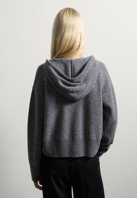 Felpa con cappuccio grigia in maglia, dal taglio morbido e rilassato, con orlo a coste e una consistenza morbida. Il cappuccio ha una forma arrotondata con dettagli delle cuciture.