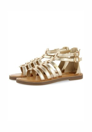 Sandalias de cuero metálico dorado con un diseño de múltiples correas, hebillas ajustables, suela plana y un acabado liso y brillante.