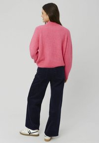 Pull en laine rose flou avec un ourlet et des poignets côtelés, associé à un pantalon large en velours côtelé marine foncé et des baskets blanches avec des accents noirs.