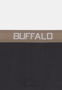 Svarte bomulls-truser med en beige elastisk midjebånd som har teksten "BUFFALO" i hvitt. Sømdetaljer er synlige på kroppen.