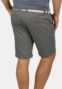 Grijze katoenen shorts met omgeslagen zomen, twee achterzakken en een bruin logo-label. Gelijkmatig afgebonden met een lichtgekleurde gevlochten riem.