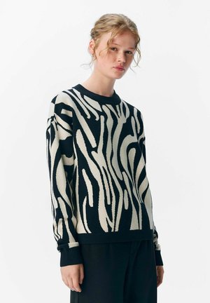 Pull rayé noir et crème avec une coupe décontractée, des manches longues et un tissu texturé. Possède un col rond et des poignets côtelés.