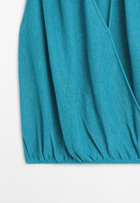 Tissu tricoté turquoise avec un ourlet élastique froncé et un motif superposé en forme de V dans le coin supérieur droit.
