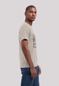 Beige katoenen t-shirt met korte mouwen, met een zwart grafisch ontwerp op de voorkant. Gekleed met blauwe denim jeans, die een aangesloten vorm laten zien.