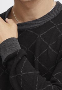 Zwart gebreid sweater met een ruitpatroon, grijze geribde halslijn en manchetten. Zachte textuur met contrasterende accenten op de mouwen.