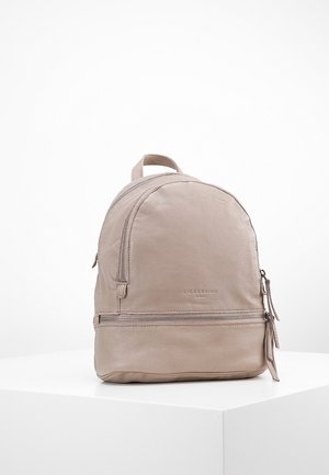 Zaino in pelle color taupe chiaro. Presenta una forma arrotondata, manico superiore, tasca frontale con zip e texture liscia con dettagli del logo sottili.