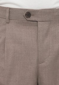 Καφέ παντελόνι σε στενή γραμμή από υφασμάτινη υφή. Διαθέτει κλείσιμο με ένα κουμπί, θηλιές για ζώνη και εμπρόσθιες πλαϊνές τσέπες.