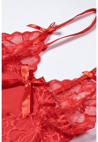 Red lace lingerie with satin ribbon accents, featuring floral patterns and sheer texture, designed with adjustable straps.