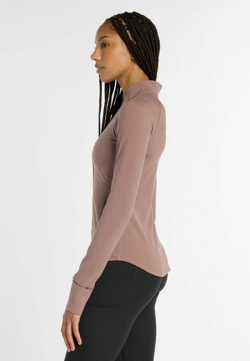 Top de manga larga en color malva claro con cuello alto y diseño ajustado. Textura suave y lisa, combinado con Leggings negros. Sin patrones ni acentos.