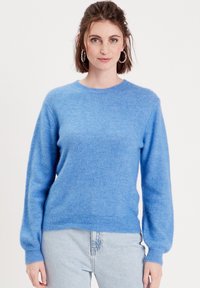 Pull en maille bleu clair fait d'un matériau doux et pelucheux. Présente un col rond, des manches longues et un ourlet côtelé. Porté avec un jean en denim clair.