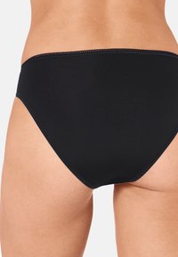 Zwarte bikinibroek met een gladde textuur, hoge uitsnijdingen aan de zijkanten en een decoratieve smalle tailleband. Heeft minimale stikdetails.