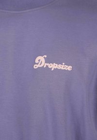 Lilla bomulds t-shirt med en blød tekstur, der har et lyserødt logo, der står "Dropsize" i et legende skrifttype.
