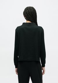 Czarna bluzka z długim rękawem wykonana z miękkiej tkaniny; posiada kołnierzyk, luźny krój z lekko skróconym dołem i teksturowanymi akcentami.