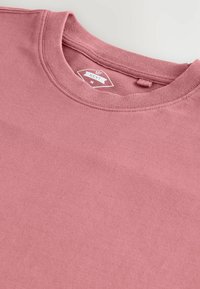 Kortärmad t-shirt med rund halsringning i dammig rosafärgad bomullsmaterial, med ribbad krage och tvätta etikett sydd inuti halsringningen.