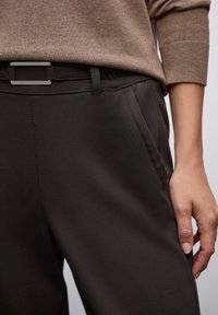Ciemnobrązowe spodnie o gładkiej fakturze, z płaskim pasem, bocznymi kieszeniami i elegancką metalową klamrą.