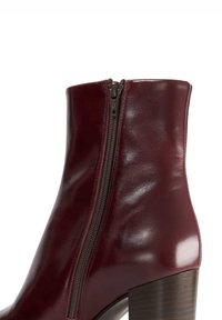 Burgundy leather ankle boot with a side zipper, high heel, and smooth texture, featuring a rounded toe and a wooden heel.