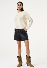 Crème gebreide trui met een textuurpatroon, zwarte leren shorts en bruine cowboylaarzen met bloemengebreide en puntige neuzen.