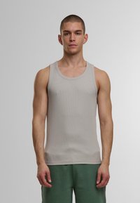 Hellgraues, geripptes Tanktop mit rundem Halsausschnitt und breiten Trägern, kombiniert mit grünen Jogginghosen. Keine auffälligen Muster oder Akzente.