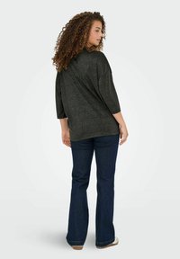 Sort, løstsiddende sweater med trekvartærmer, struktureret stof og rund halsudskæring, parret med brede mørke denim bukser.