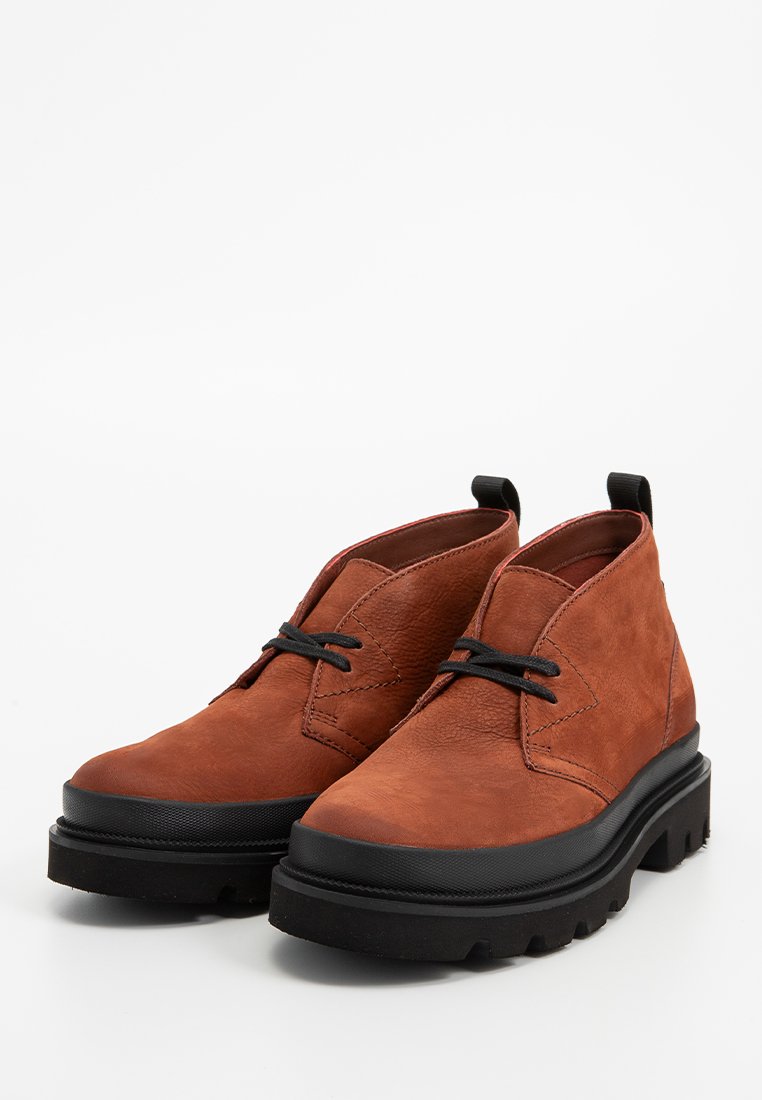 Bottines en cuir marron avec une finition texturée, semelle en caoutchouc noir et lacets noirs. Présentent un design minimaliste et un talon légèrement surélevé.