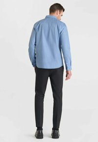 Lichtblauw button-up overhemd met een gestructureerd patroon, gecombineerd met slanke zwarte broek en zwarte schoenen, gezien vanuit de achterkant.