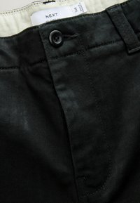 Čierne bavlnené nohavice so striedmym strihom, s hladkou textúrou, s uzáverom na gombík a štítkom vo vnútri, ktorý obsahuje informácie o veľkosti a značke.