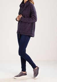 Felpa viola, con texture e colletto a scialle, tasca frontale e fessure laterali. Abbinata a jeans scuri e sneaker grigie.