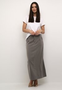 Gray maxi skirt with a straight silhouette, featuring front pleats, paired with a white short-sleeve t-shirt and beige high heels.