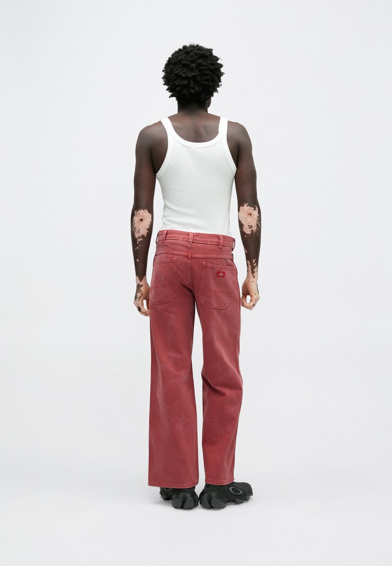 Red wide-leg jeans with a worn texture, featuring two back pockets and a small logo near the waist, paired with a white tank top.