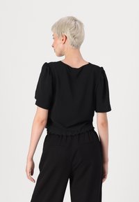Top preto com mangas bufantes, decote arredondado e barra rendada. Feito de um tecido macio, tem um corte descontraído e mangas curtas.