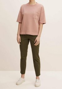 Ljusrosa kortärmad t-shirt med bröstficka, kombinerad med olivgröna avsmalnande byxor och vita sneakers. Slät textur och avslappnad passform.