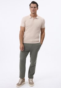 Polo de manga corta beige con un patrón texturizado, combinado con pantalones verde claro y zapatillas beige. Diseño casual y ajustado en todo.