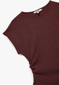 Burgundy tekstuuri tipp ümara kaelusega ja lühikeste varrukatega, külgedel on kogumise detailid. Valmistatud pehmest, venivast materjalist.