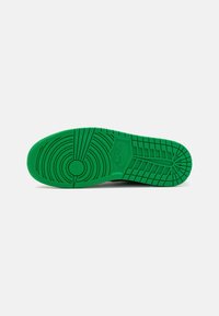 Semelle d'une basket Nike verte avec des motifs de bande de roulement circulaires et linéaires sur un fond gris clair.