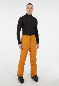 Oranje skibroek met een rechte snit, voorzien van een knoop- en ritsluiting, en zijzakken. Gecombineerd met een aansluitend zwart longsleeve shirt.
