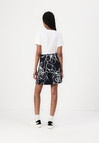 Ein weißes kurzärmliges Hemd und einen dunkelblauen Rock mit weißen Blumenmustern. Das Outfit umfasst weiße Sneakers mit schwarzen Akzenten und Knöchelsocken.