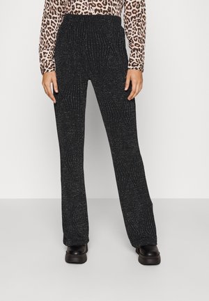 Zwarte broek met rechte pijpen en zilveren glitterpatroon, gecombineerd met zwarte plateauzolen en een lange mouw top met luipaardprint.