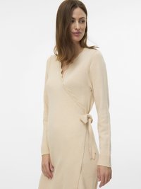 Vaaleanbeige kietaisumekko, jossa on aaltoileva V-aukko, pitkät hihat ja solmittava vyötärö. Pehmeä tekstuuri ja neulottu kangas, jossa resorit hihansuissa.