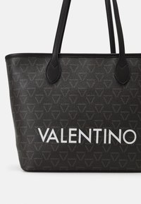 Black tote bag with smooth textured surface, featuring embossed logo pattern and bold white "VALENTINO" text on the front. Double handles.