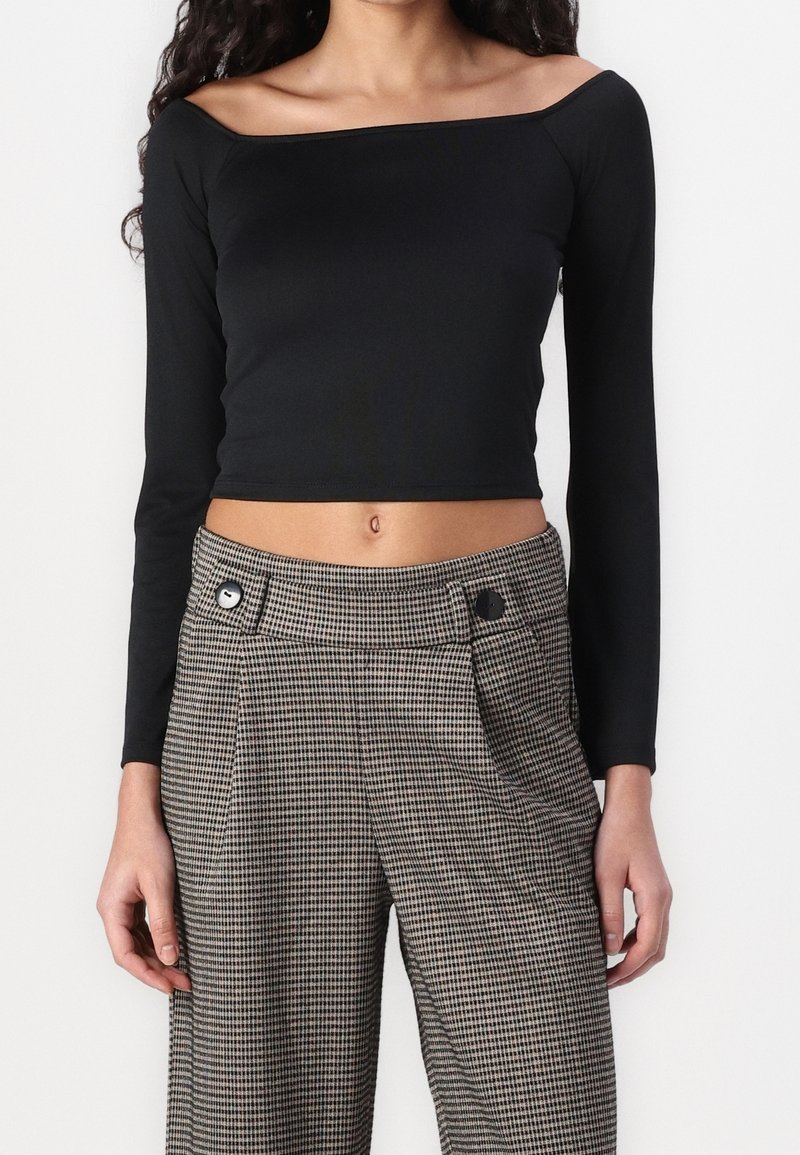 Musta tiukka pitkähihainen crop-top, jossa on kyljistä paljastava malli, yhdistettynä korkeavyötäröisiin ruudullisiin housuihin, joissa on kaksi nappia.