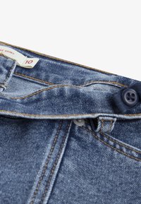 Svijetloplave traperice s kopčanjem na gumb i zatvaračem. Imaju šivane šavove i oznaku "10". Teksturirana tkanina s izblijedjelim finišem.