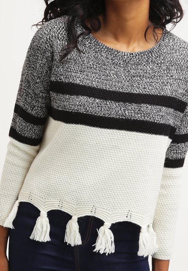 Pull en tricot avec un motif rayé gris et noir, corps blanc texturé, et pompons décoratifs à l'ourlet.