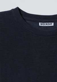 Marineblauw katoenen T-shirt met een ronde hals en geribbelde rand. Label met de tekst "WEEKDAY" aan de binnenkant van de kraag. Zachte, gestructureerde stof.
