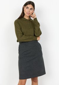 Olivgrön långärmad polo med knäppning och grå texturerad blyertskjol. Enkelt, skräddarsytt design med en figuretad siluett.