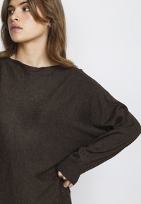 Maglione marrone all'uncinetto con una vestibilità ampia e scollatura larga. Presenta polsini a costine e una consistenza morbida, progettato per il comfort e la facilità di movimento.