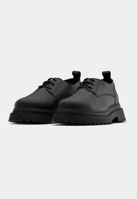 Μαύρα δερμάτινα παπούτσια με υφασμάτινη επιφάνεια, στρογγυλή μύτη, χοντρή καουτσούκ σόλα και σχέδιο με κορδόνια; διαθέτει μια θηλιά στην φτέρνα.