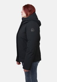 Giacca nera isolata con cappuccio e logo sulla manica sinistra, dotata di tasche con cerniera e design strutturato e aderente.