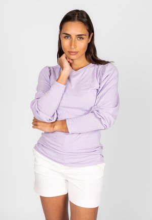 Lange mouwen, licht lavendelkleurig top met opgezette schouders en ronde hals, gecombineerd met witte shorts. Zachte textuur, casual pasvorm.