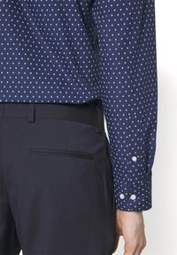 Camicia a righe blu navy con motivi a rombi, maniche lunghe e polsini con bottoni, abbinata a pantaloni scuri con una tasca posteriore elegante.